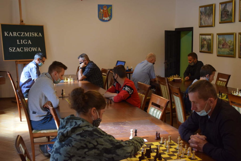 Zbliżenie na grających w szachy. Na pierwszym planie dwóch uczestników, jeden odwrócony tyłem. W tle pozostali gracze.