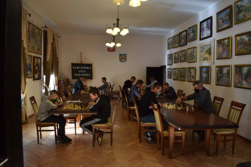Na zdjęciu widoczna jest cała sala. Przy stołach ustawionych w dwóch rzędach siedzą grający w szachy zawodnicy.