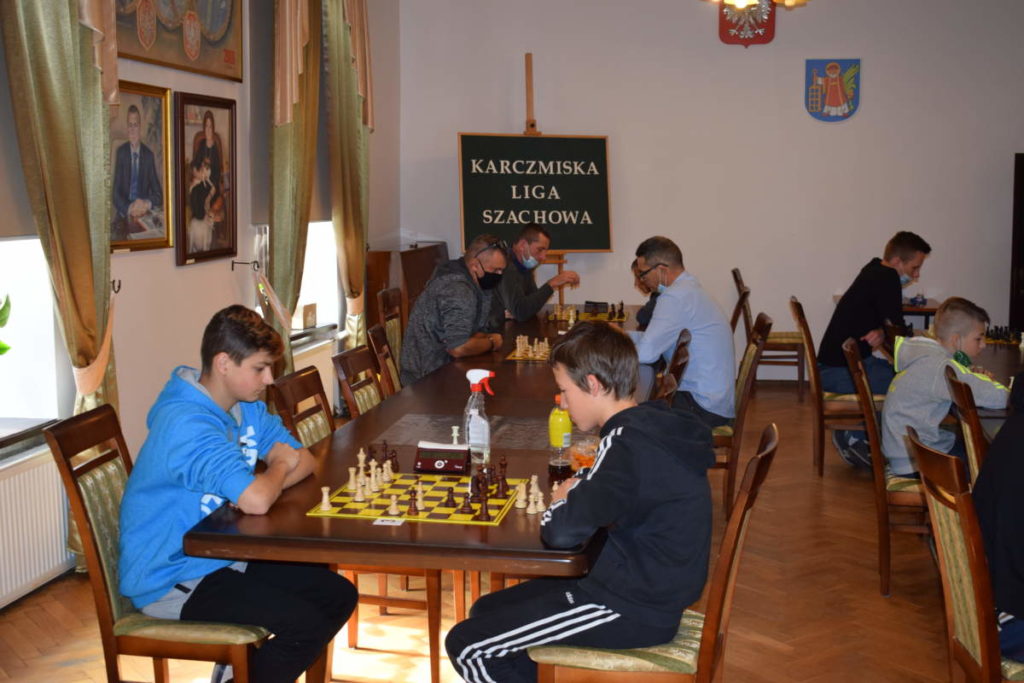 Zbliżenie na jeden stół. Na pierwszym planie dwóch uczestników rozgrywa partię szachów. W tle widoczni pozostali gracze.