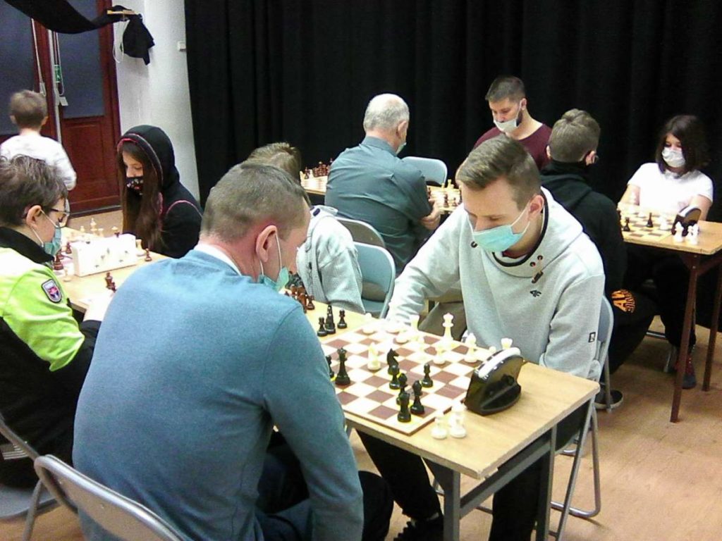 Na zdjęciu wzdłuż dwóch rzędów stołów siedzą zawodnicy grający w szachy.