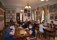 Na zdjęciu widoczna jest cała sala. Przy stołach ustawionych w dwóch rzędach siedzą grający w szachy zawodnicy.