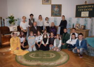 Zdjęcie grupowe uczestników Narodowego Czytania. Niektórzy siedzą wokół dywanu, kila osób stoi z tyłu. Wszyscy ubrani w stroje z epoki.
