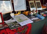 Materiały promocyjne leżą na stole przykrytym zielonym obrusem i kolorową chustą.