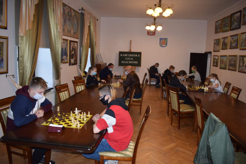 Zdjęcie całej sali. Widać dwa rzędy stołów, przy których trwają rozgrywki szachowe.