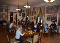 Widok na całą salę. Widać dwa rzędy stołów, przy których uczestnicy turnieju grają w szachy.