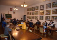 Widok na całą salę. Widać dwa rzędy stołów, przy których uczestnicy turnieju grają w szachy. Na ścianie wiszą obrazy.