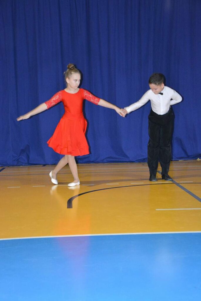 Na zdjęciu widoczna para tańcząca para dzieci. Dziewczynka jest w czerwonej sukience, chłopiec w czarnych spodniach i białej bluzce.