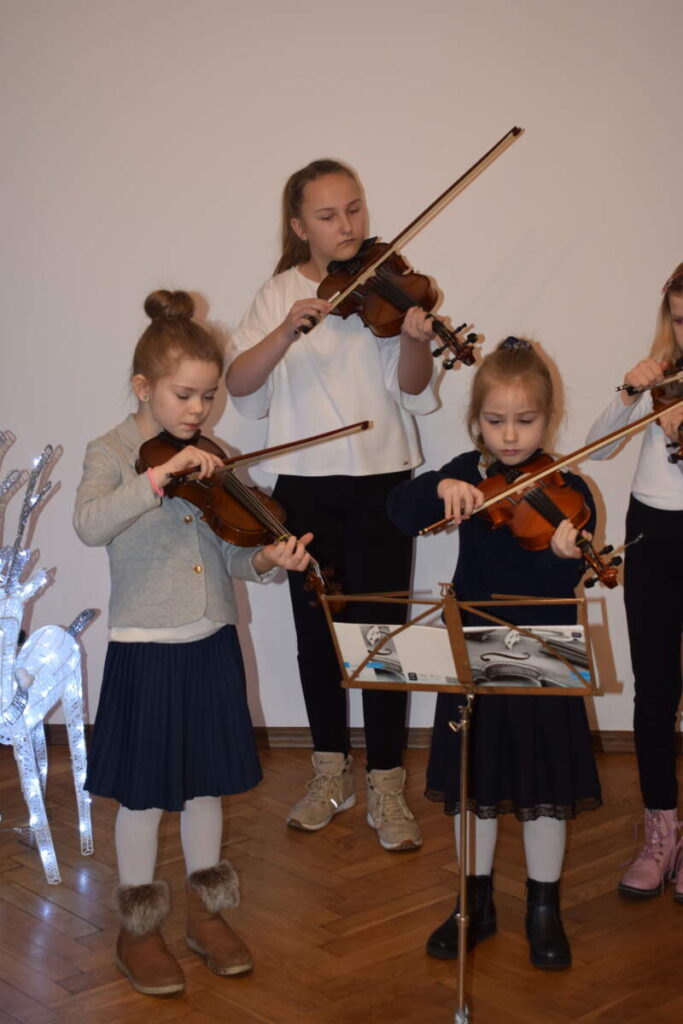 Na zdjęciu troje dzieci gra na skrzypcach.