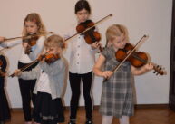 Na zdjęciu czworo dzieci gra na skrzypcach.