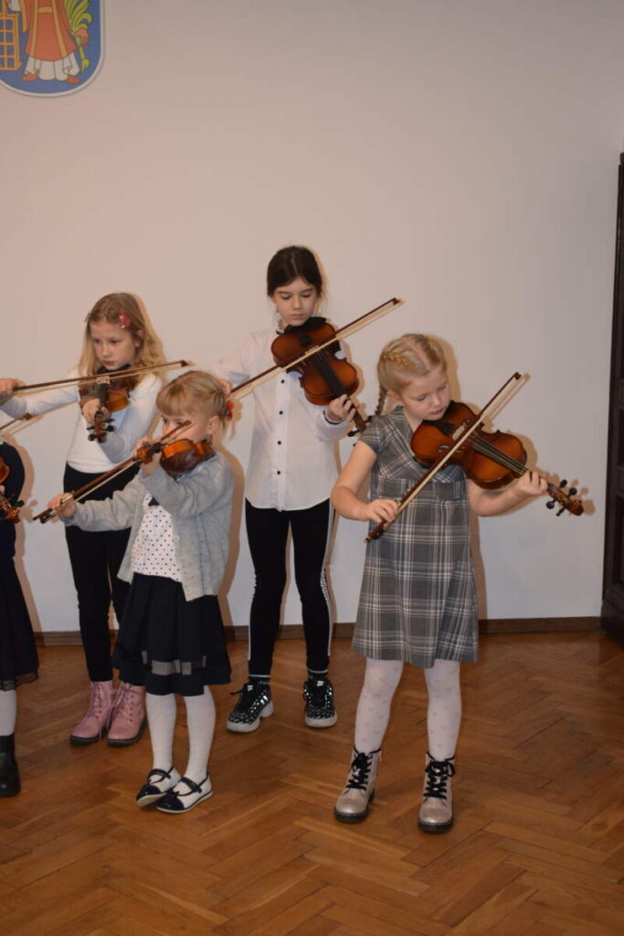 Na zdjęciu czworo dzieci gra na skrzypcach.