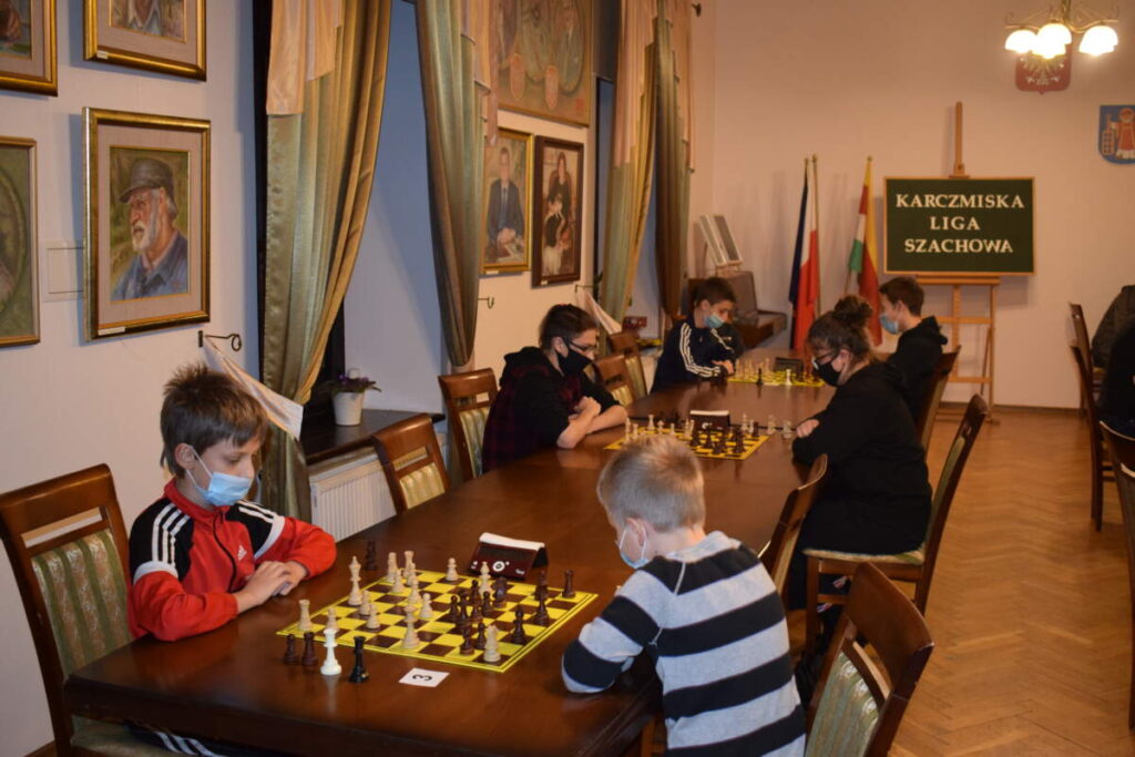 Przy rzędzie stołów ustawionych przy oknie zawodnicy grają w szachy.
