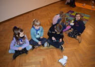 Na podłodze siedzi grupka dzieci. Przed nimi stoi robot.