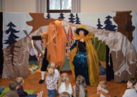 Aktorzy ubrani w kolorowe stroje stoją przed grupą dzieci.