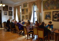 Przy rzędzie stołów ustawionych przy oknach siedzą zawodnicy i grają w szachy.