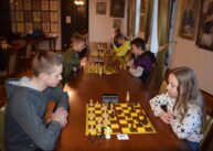 Przy rzędzie stołów ustawionych przy oknie zawodnicy grają w szachy.