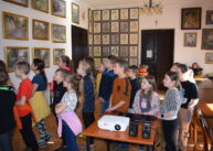 Grupa dzieci stoi i ogląda obrazy wiszące na ścianach.