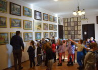 Grupa dzieci stoi i ogląda obrazy wiszące na ścianach.