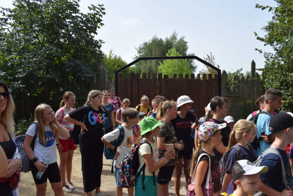 Grupka dzieci stoi obok drewnianej bramy.
