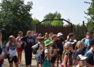 Grupka dzieci stoi obok drewnianej bramy.