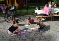 Dzieci rysują kolorową kredą na kostce brukowej.