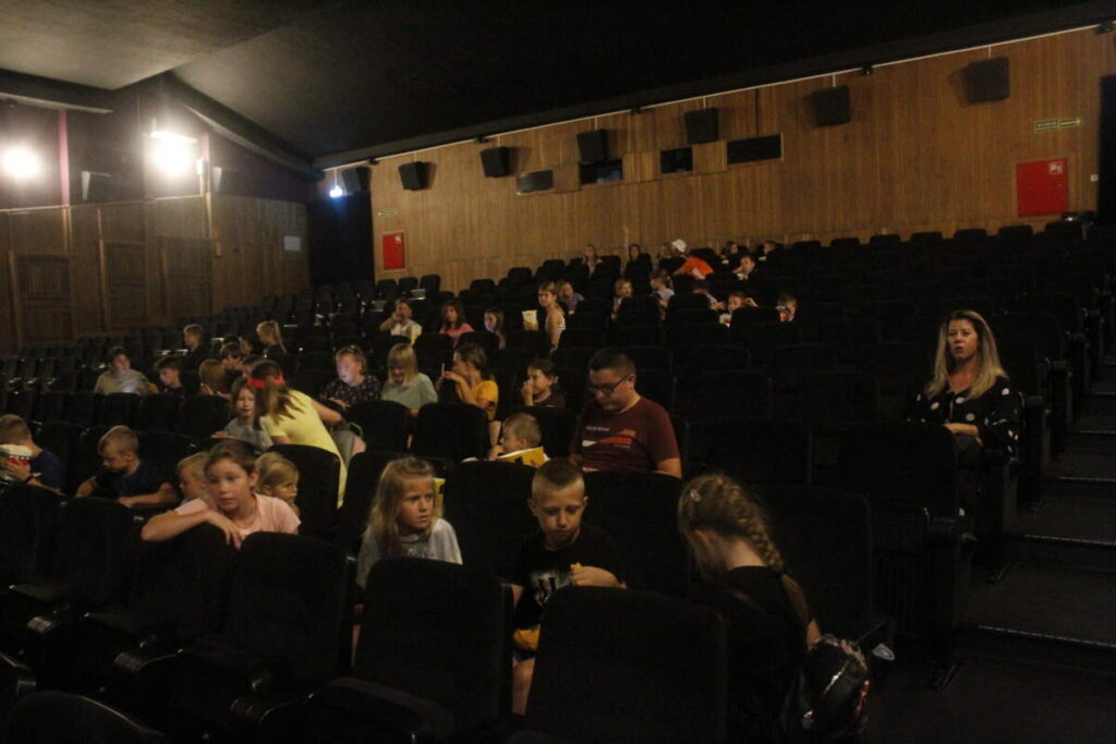 W ciemnej sali kinowej siedzi duża grupa osób.