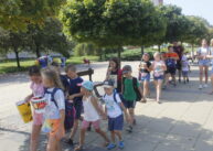 Grupa dzieci idzie rzędem wzdłuż szpaleru drzew.