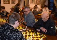 Przy stole widoczne są trzy pary zawodników grających w szachy.