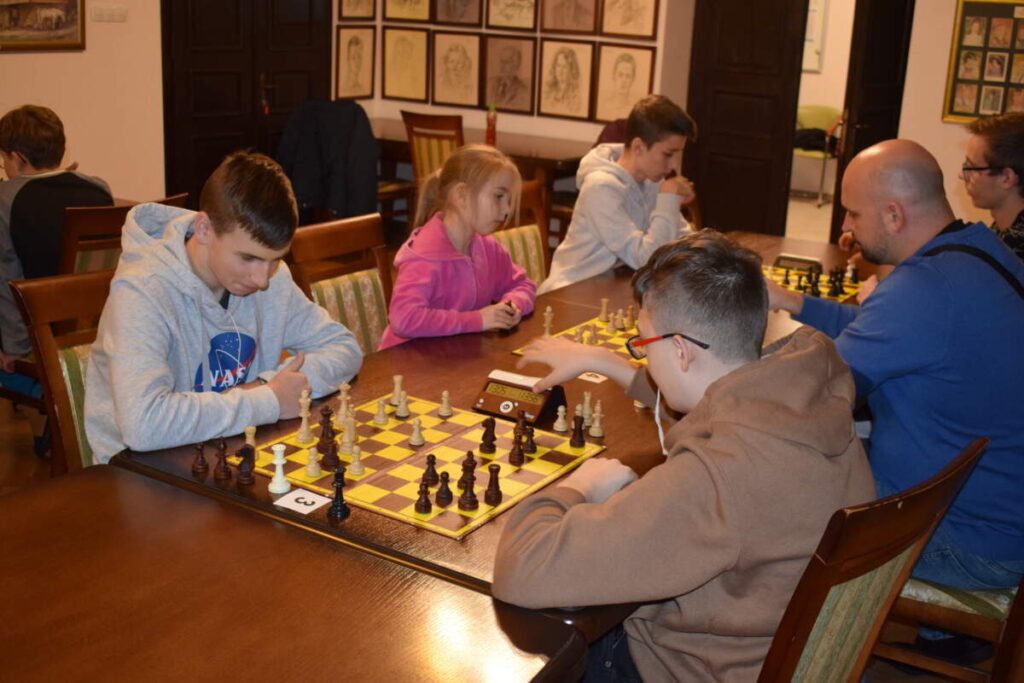 Przy stole widoczne są pary zawodników grających w szachy.