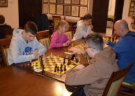 Przy stole widoczne są pary zawodników grających w szachy.