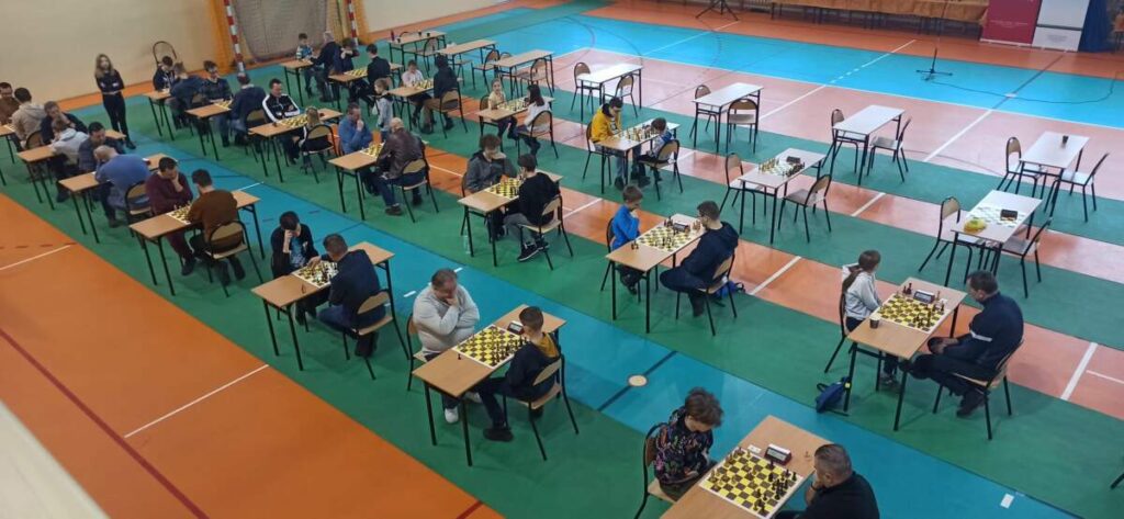 Na sali gimnastycznej, przy ustawionych rzędami stołach siedzą szachiści.