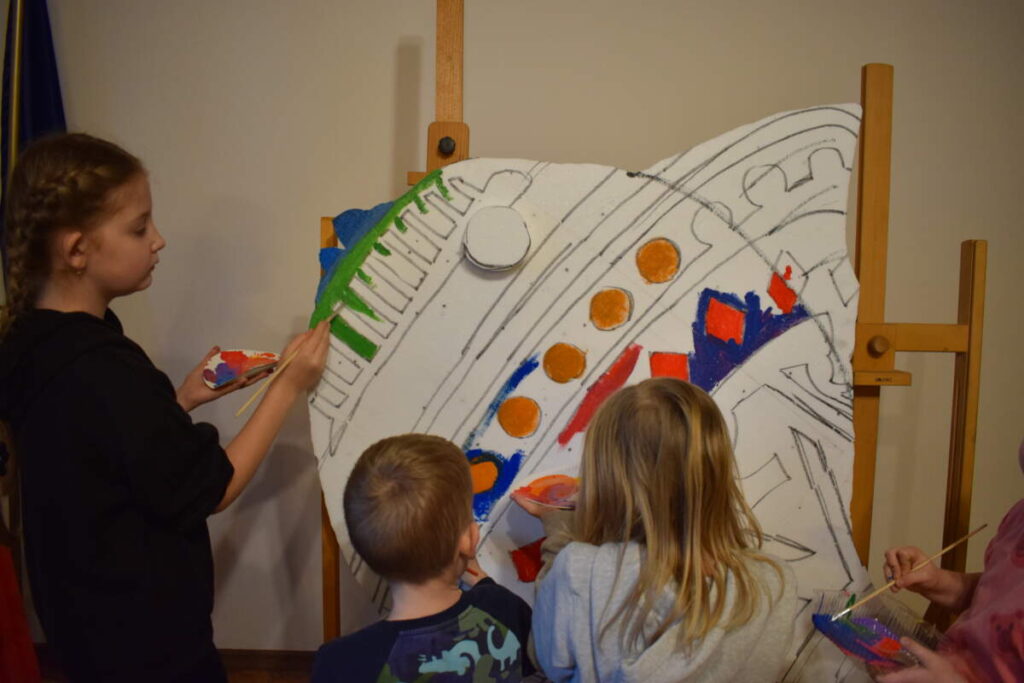 Dzieci stoją przy sztaludze i malują farbami.