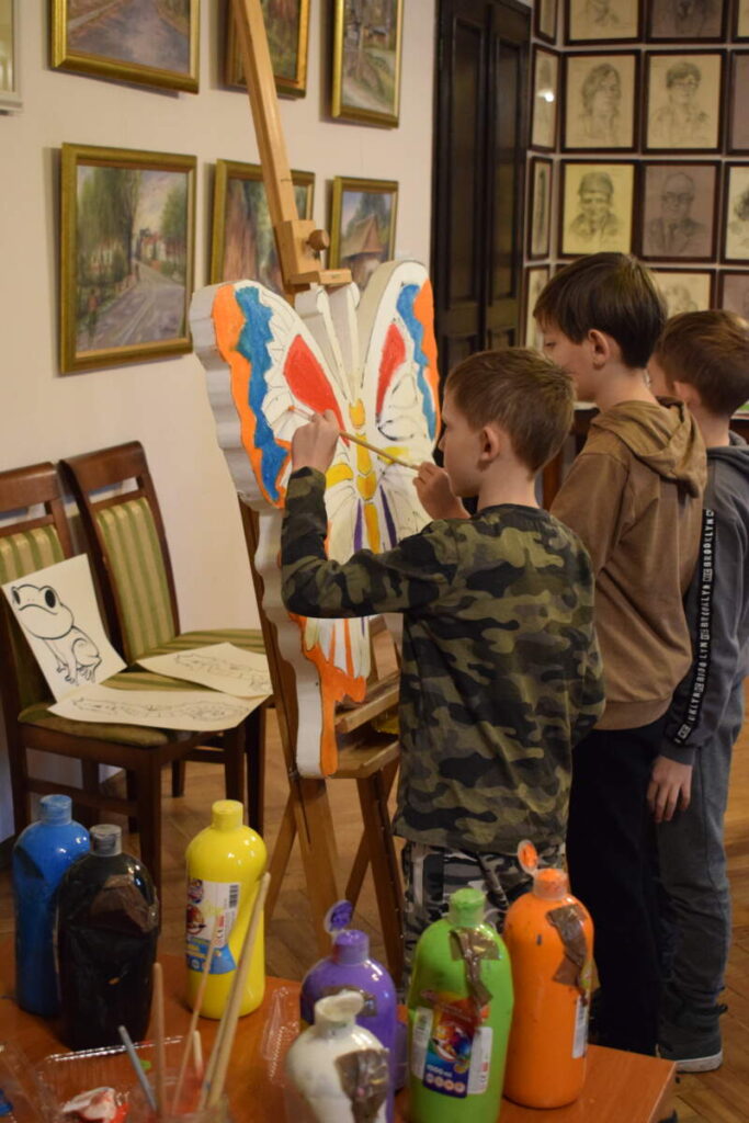Dzieci stoją przy sztaludze i malują farbami.