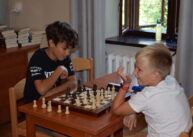 Przy stole siedzi dwoje dzieci i grają w szachy.