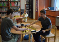 Przy okrągłym stole siedzi dwóch chłopców i gra w szachy.