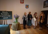 Grupa osób pozuje do zdjęcia obok stolika, na którym stoją kwiaty
